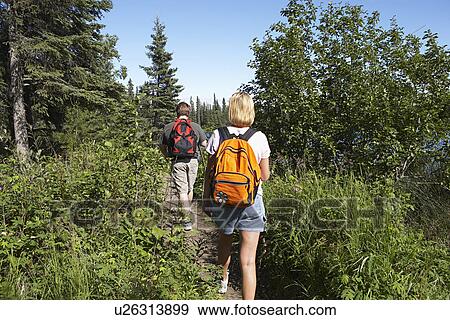 Stock Photo - USA, Alaska, couple walking along trail in forest. Fotosearch