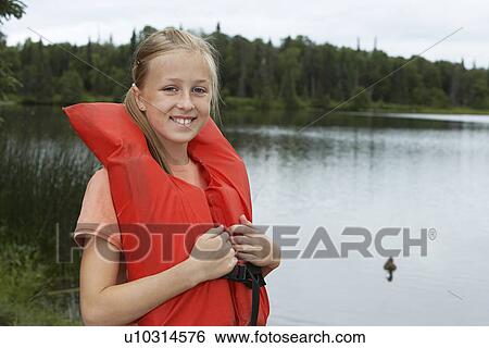Stock Photograph - USA, Alaska, teenage girl wearing life jacket by lake, portrait. Fotosearch