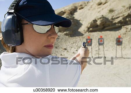 Stock Image - Woan aiming hand gun at firing range. Fotosearch
