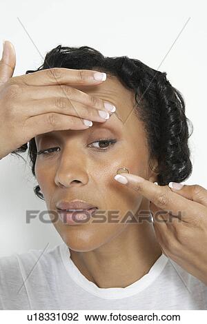 Stock Image - Woman applying contact lenses, studio shot. Fotosearch