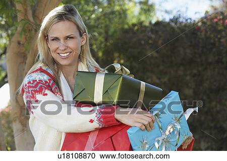 Stock Image - Woman carrying presents outside, portrait. Fotosearch