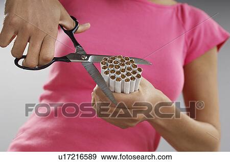 Stock Photo - Woman cutting bundle of cigarettes, close-up. Fotosearch