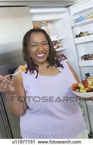 Stock Image - Woman eating salad by open fridge. Fotosearch