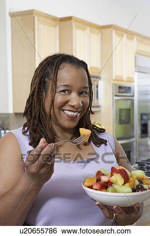 Stock Photograph - Woman eating salad in kitchen. Fotosearch