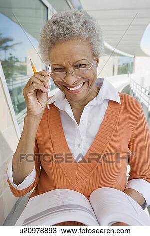 Stock Image - Woman holding book at school, smiling, portrait. Fotosearch
