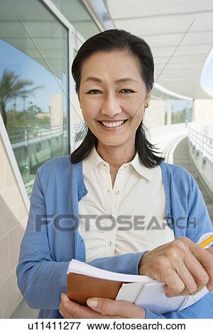 Stock Photo - Woman holding book at school, smiling, portrait. Fotosearch