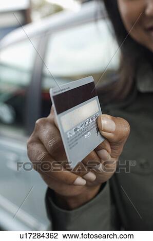 Stock Image - Woman holding credit card outdoors, focus on foreground. Fotosearch