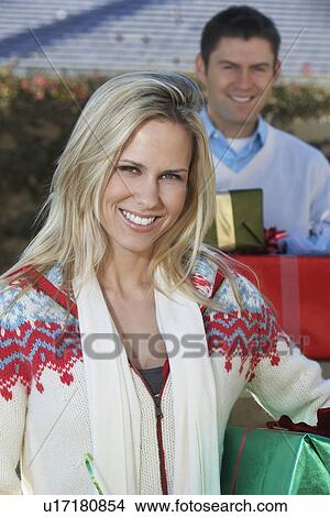 Picture - Woman holding presents outdoors with man behind. Fotosearch