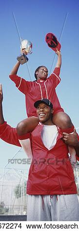 Picture - Woman holding trophy, sitting on man's shoulders, low angle view. Fotosearch