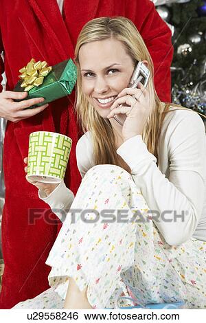 Woman in pyjamas on cell phone in front of man holding Christmas present View Large Photo Image Stock Photograph - Woman in pyjamas on cell phone in front of man holding Christmas present. Fotosearch