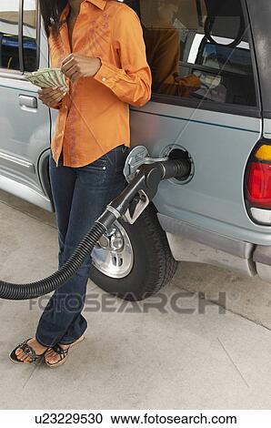 Stock Image - Woman leaning on van with fuel pump counting money, low section. Fotosearch