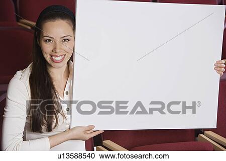 Stock Image - Woman sitting in auditorium, holding empty placard. Fotosearch