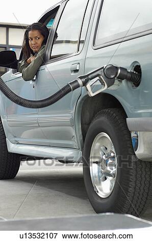 Stock Photo - Woman sitting in car looking at fuel pump. Fotosearch