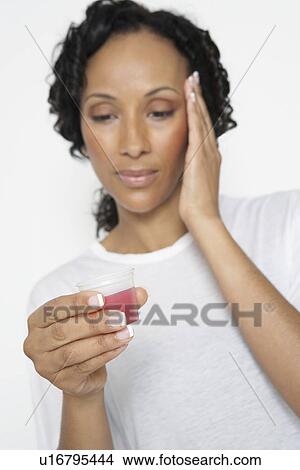 Picture - Woman taking medicine, with hand on head, close-up. Fotosearch