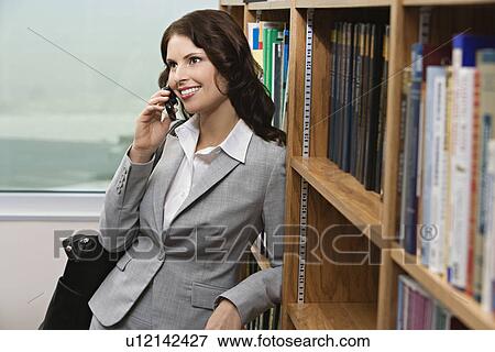 Stock Photo - Woman talking on mobile phone in library. Fotosearch