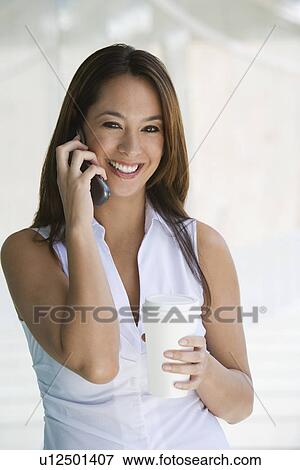 Stock Photo - Woman using cell phone holding takeout coffee, portrait. Fotosearch