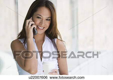 Stock Photograph - Woman using cell phone holding takeout coffee, portrait. Fotosearch