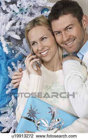 Woman using cell phone with man embracing her by Christmas tree View Large Photo Image Stock Image - Woman using cell phone with man embracing her by Christmas tree. Fotosearch
