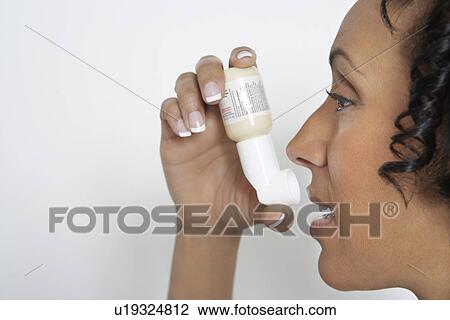 Stock Image - Woman using inhaler, studio shot. Fotosearch