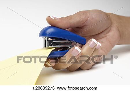 Stock Image - Woman using stapler, close-up of hand. Fotosearch
