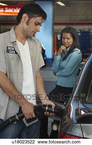 Stock Image - Woman watching gas station attendant pumping gas. Fotosearch