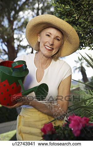 Stock Image - Woman watering flowers in garden. Fotosearch