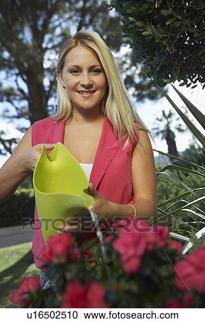 Stock Image - Woman watering flowers in garden. Fotosearch