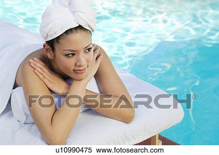 Stock Photography - Young Chinese woman lying by swimming pool. Fotosearch