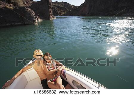 Stock Image - Young couple embracing in boat on lake, portrait. Fotosearch