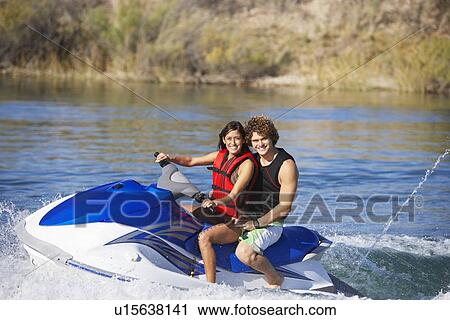 Stock Image - Young couple riding jetski on lake, portrait. Fotosearch