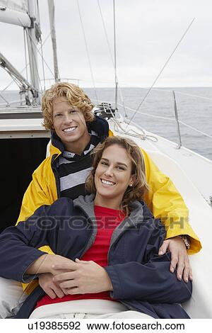 Stock Image - Young couple smiling on sailboat, portrait. Fotosearch