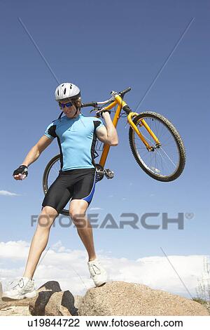 Young man carrying bicycle on rocks View Large Photo Image Stock Image - Young man carrying bicycle on rocks. Fotosearch