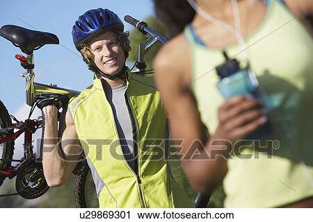 Stock Image - Young man carrying bicycle, outdoors, portrait. Fotosearch