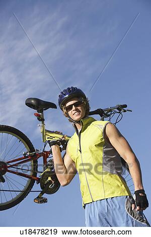 Young man carrying bicycle, outdoors, portrait View Large Photo Image Stock Photo - Young man carrying bicycle, outdoors, portrait. Fotosearch
