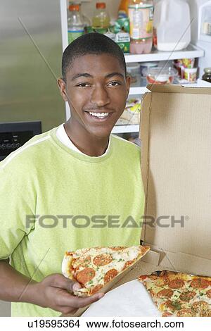 Young man eating pizza at home View Large Photo Image Picture - Young man eating pizza at home. Fotosearch