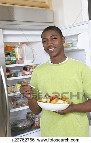 Stock Photograph - Young man eating salad by open fridge. Fotosearch