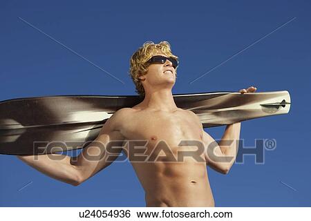 Stock Photograph - Young man holding wakeboard outdoors, low angle view. Fotosearch