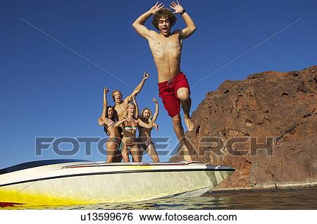 Stock Photograph - Young man jumping from boat, friends watching in background. Fotosearch