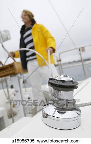 Stock Photography - Young man on yacht in sea, focus on crank with rope. Fotosearch