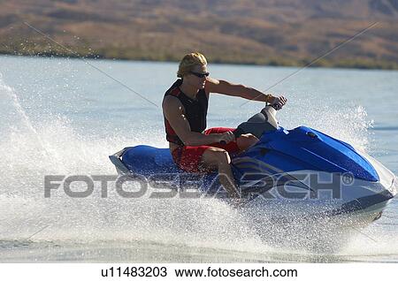 Stock Image - Young man riding jetski on lake. Fotosearch