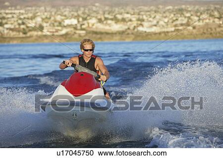 Stock Image - Young man riding jetski on lake. Fotosearch