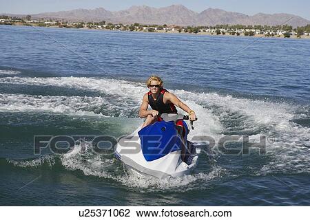 Stock Image - Young man riding jetski on lake. Fotosearch