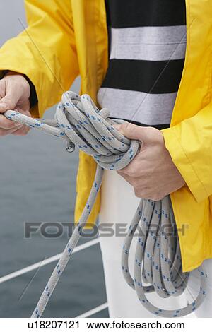 Stock Image - Young man tying rope on yacht, mid section. Fotosearch