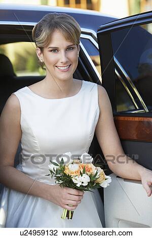 Stock Image - Young woman holding bouquet in open door of limousine, portrait. Fotosearch