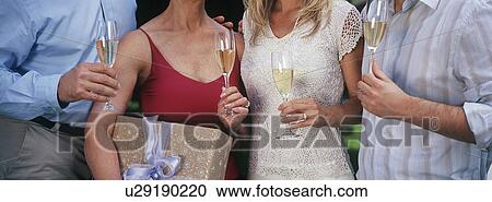 Stock Image - Young woman holding present, with friends drinking champagne, mid section. Fotosearch