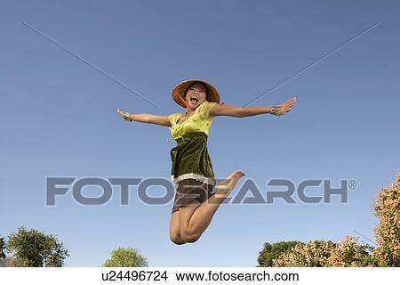 Picture - Young woman jumping in park, side view. Fotosearch