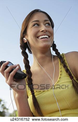 Stock Image - Young woman listening to mp3 player. Fotosearch
