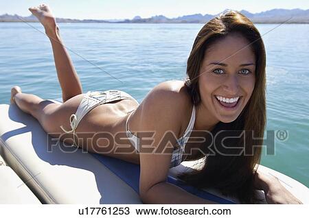 Stock Image - Young woman relaxing on boat, smiling, portrait. Fotosearch