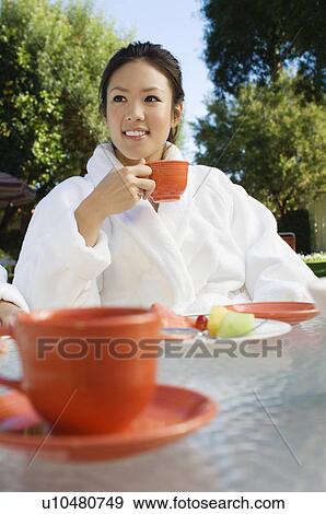 Young woman wearing bathrobe, drinking at outdoor table View Large Photo Image Stock Photo - Young woman wearing bathrobe, drinking at outdoor table. Fotosearch