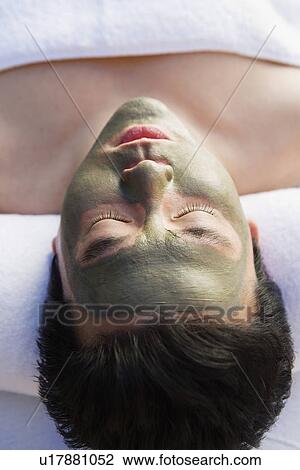 Stock Image - Young woman wearing mud facial mask at health spa, close-up. Fotosearch